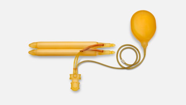Top-down photograph of a three-piece inflatable penile prosthesis: two cylinders, scrotal pump and fluid reservoir on a neutral background